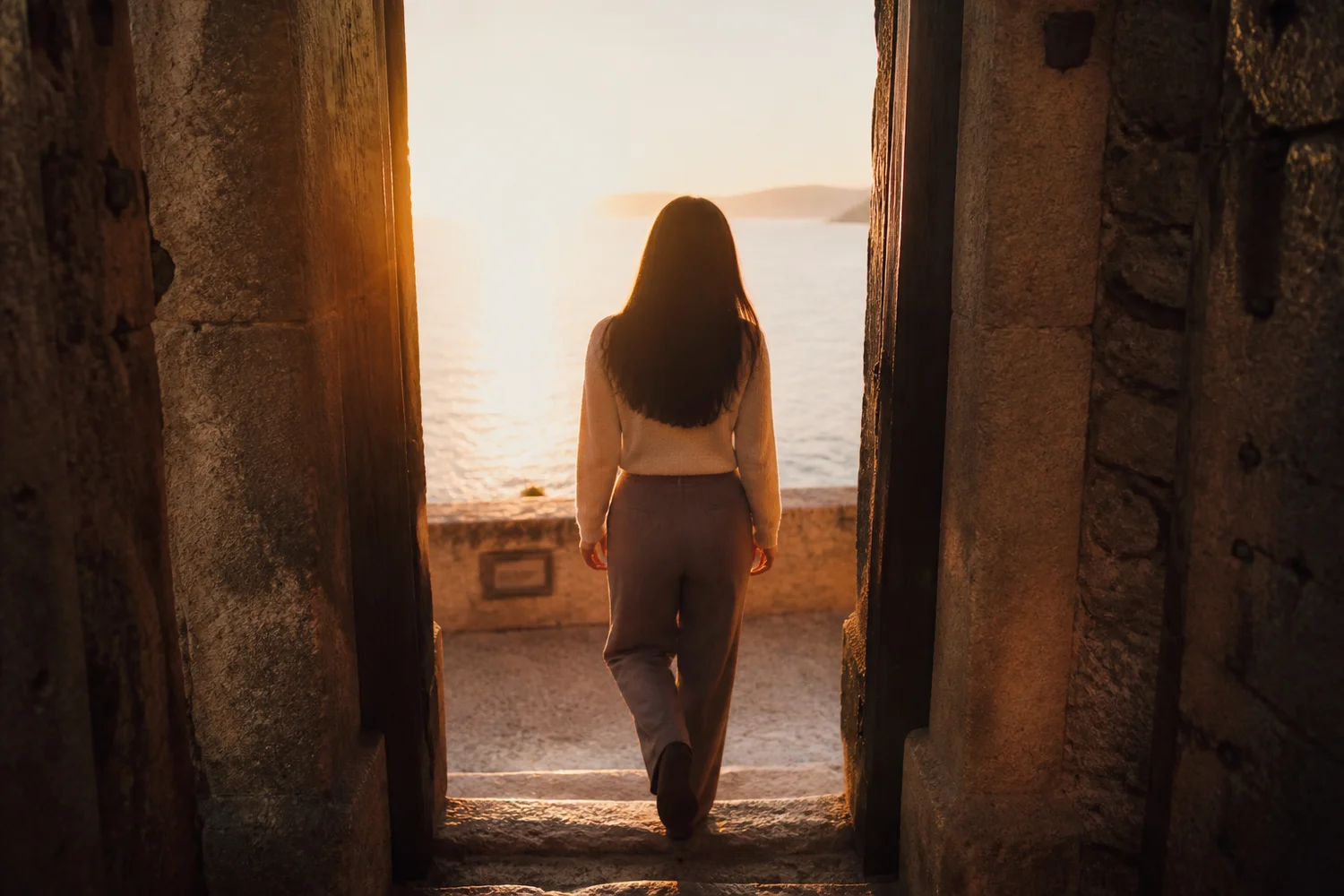 Une femme monte deux marches de pierre vers une porte ouverte sur l'aube.